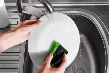 Kadın yemekten sonra lavaboda bulaşık yıkıyor. Kadın tabağı yıkıyor.