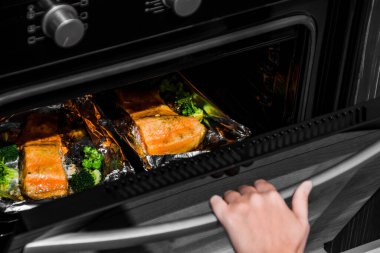 Kadın fırını açar. Elini fırın kapağına koy. Fırında alabalık. Kadın fırında somon balığı pişiriyor..