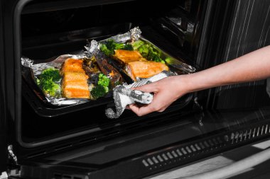 Kadın fırını açar. Elini fırın kapağına koy. Fırında alabalık. Kadın fırında somon balığı pişiriyor..