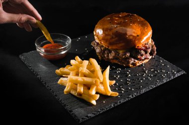 Adamın eli ketçaplı patates kızartması tutuyor. Kızlar hamburger yer. Fast food. Amerikan mutfağı.