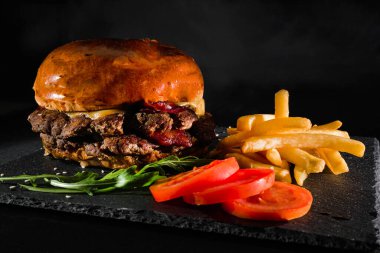 Patates kızartması ve domatesli siyah tabakta hamburger. Makro. Fast food. Amerikan mutfağı.