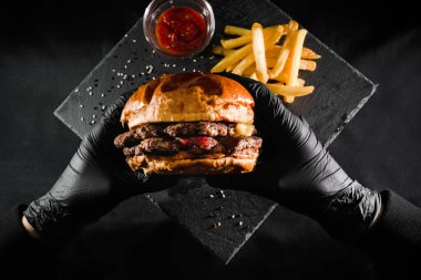 Siyah eldivenli bir adam hamburger tutuyor. Çizburger yiyen bir kadın. Üst Manzara. Fast food. Amerikan mutfağı.
