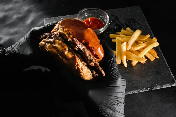 a man in black gloves holds a burger. woman eating a cheeseburger. top view. fast food. american cuisine