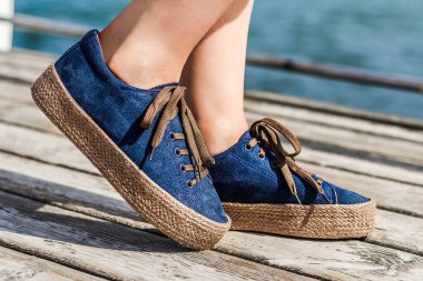 Kızlar ve kadınlar için mavi süet espadrilles. Ahşap arka planda rahat, modaya uygun ayakkabılar giymiş kadın bacakları. Şık ayakkabılar, SS '20.