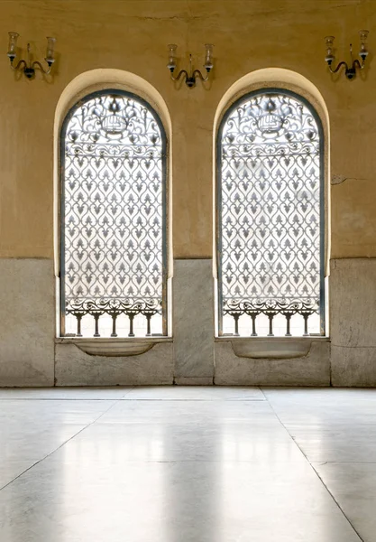 Zwei eiserne kunstvolle Fenster über gelber Steinmauer und weißem Marmor — Stockfoto