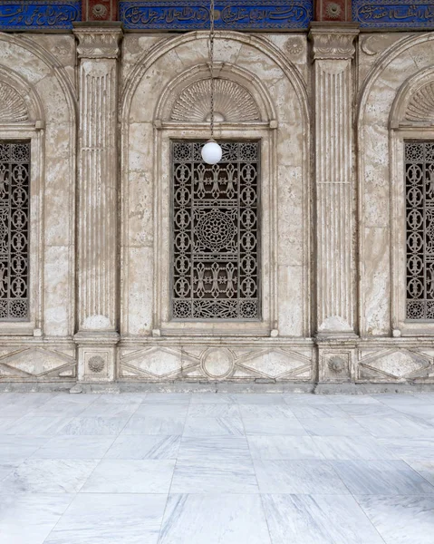 Three adjacent arched windows with decorated iron grid over white marble decorated wall