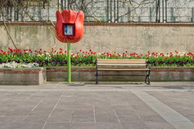 Lale şeklinde genel telefon ve yerleşik Lale çiçek kutusu ve grunge duvara döşeli taş zemine önünde ahşap Bank
