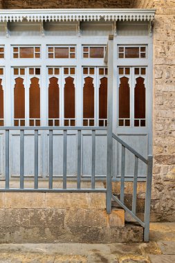 Taş duvar, mavi Ahşap korkuluk ve taş merdivenle üzerinde sarı camlı ahşap mavi kapı dizisi