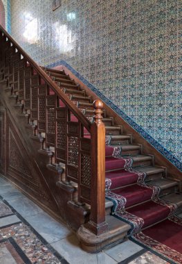 Artan bir süslü kırmızı halı ile ahşap merdiven, Ahşap korkuluk ve Türk Seramik duvar dekore edilmiştir