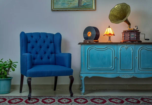 Sillón azul, aparador azul claro de madera vintage, lámpara de mesa antigua iluminada, fonógrafo antiguo (gramófono), discos de vinilo en el fondo de la pared beige, suelo de porcelana alicatada y alfombra roja — Foto de Stock