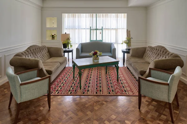 Sala de estar moderna de lujo con tres sofás, dos sillones y mesa de madera vintage en el fondo de una gran ventana con cortinas blancas y alfombra decorada en el suelo de barquet — Foto de Stock