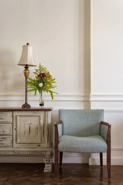 Sillón azul claro y barra lateral vintage crema con lámpara de mesa y maceta de flores en la pared de color blanco hueso y piso de madera — Foto de Stock