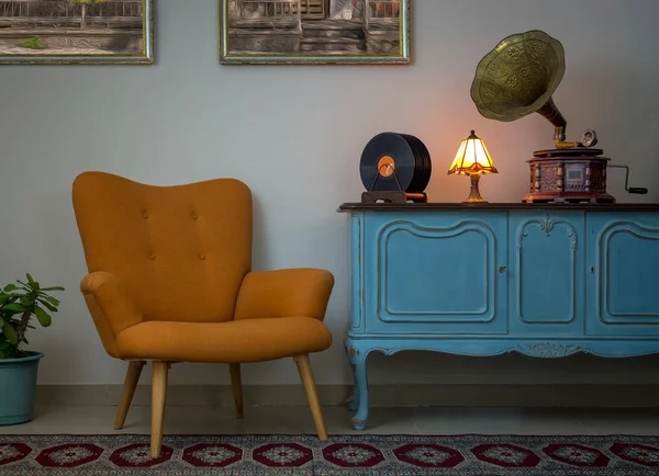 Interior vintage de sillón retro naranja, aparador vintage azul claro de madera, fonógrafo antiguo (gramófono), discos de vinilo y lámpara de mesa iluminada — Foto de Stock