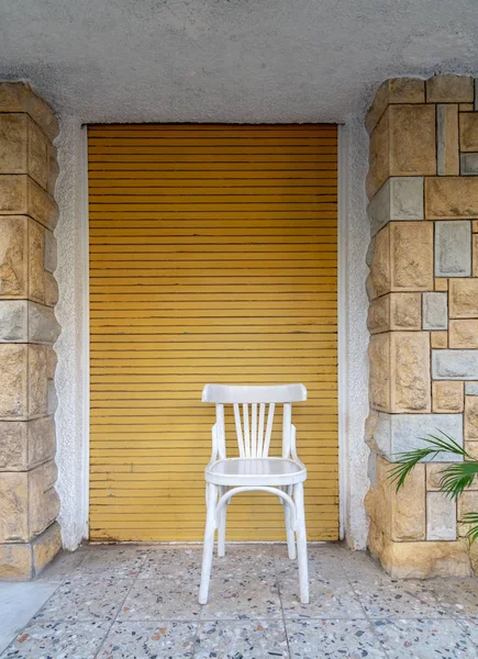 Traditional Egyptian white wooden chair over in front of bricks stone wall and yellow roll-up door — Stock Photo, Image