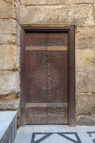 Wooden ornate door with geometrical engraved patterns on external old decorated bricks stone wall — Stock Photo, Image