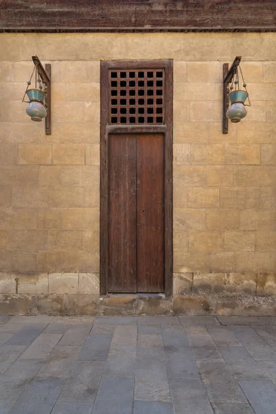 Puerta cerrada de madera y faroles de calle de vidrio árabe colgados en un poste de madera en la pared de ladrillos de piedra viejos —  Fotos de Stock