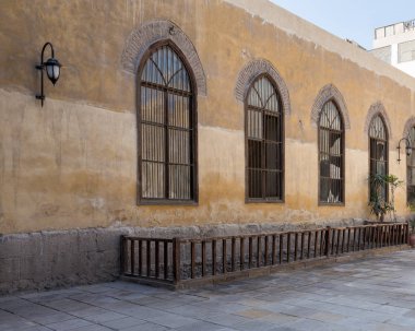 Tahta kemerli pencere, dövülmüş demir ızgara, sarı taş tuğlalar duvar ve ahşap kiriş.