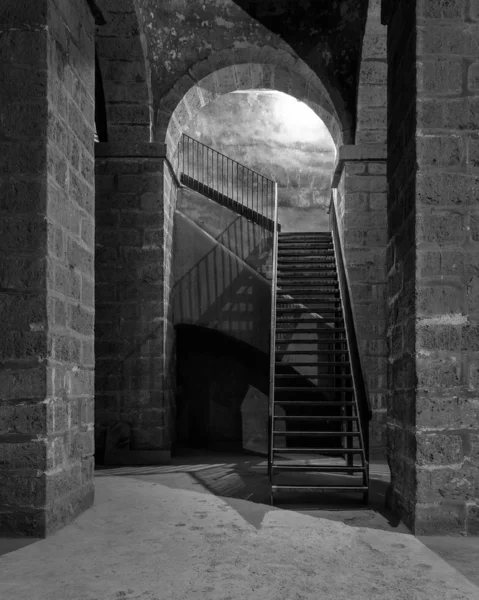 Черно-белый темный заброшенный подземный ход с каменными кирпичными колоннами и металлической лестницей — стоковое фото