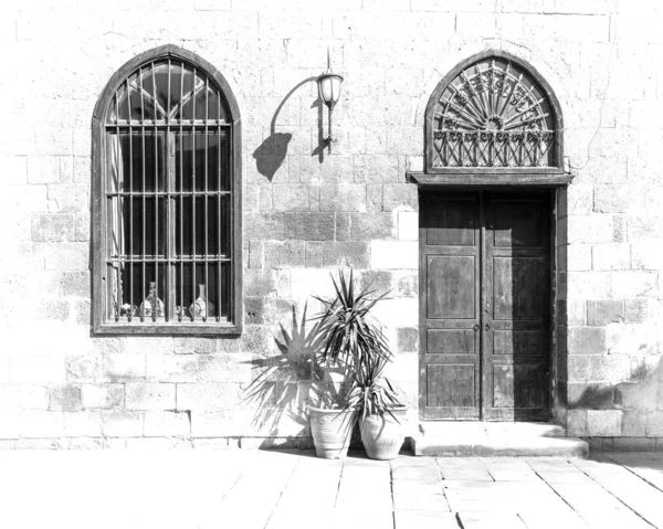 Черно-белый высокий контраст кирпичной стены с деревянной дверью и кованым железным окном в солнечный день — стоковое фото
