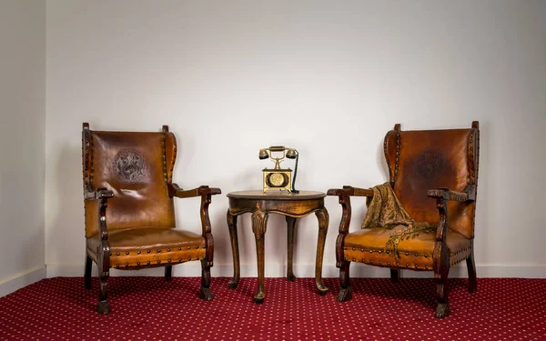 Dos sillones de madera, una pequeña mesa de café y un viejo teléfono — Foto de Stock
