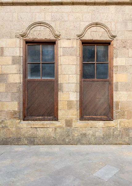 Parede de tijolos de pedra abandonada velha decorada com duas janelas de persianas de madeira arqueadas — Fotografia de Stock