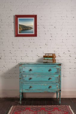 Beyaz tuğlalı duvar, eski moda turkuaz bir dolap ve asılmış bir resim.