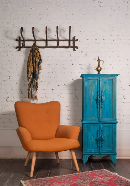 Sillón wingback naranja francés, armario vintage y percha de pared con bufanda adornada en la pared de ladrillos — Foto de Stock