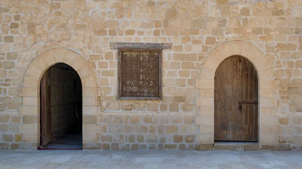 Two weathered wooden arched doors and closed rusted wrought iron window on bricks stone wall