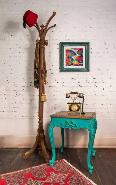 Mesa auxiliar vintage de madera, teléfono antiguo dorado y soporte de percha con fez rojo y bufanda — Foto de Stock