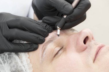 Erkekler için bir güzellik salonunda mikropatenli kaş dövme prosedürü.