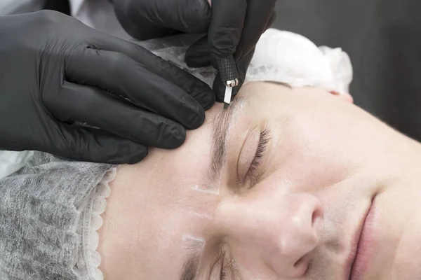 Microblading eyebrow tattoo procedure in a beauty salon for men