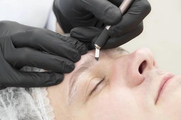 Microblading eyebrow tattoo procedure in a beauty salon for men