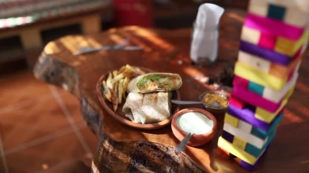 Tiro de un delicioso burrito vegano junto a la colorida torre de Jenga sobre la mesa rústica — Vídeo de stock