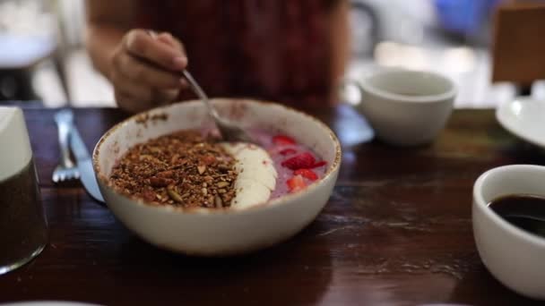 Shot van het eten van een Smoothie Bowl met Granola en aardbeien met zwarte koffie — Stockvideo