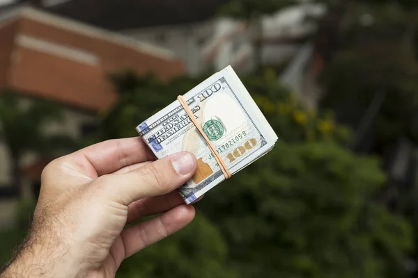 Hand eines Mannes mit Dollarscheinen vor einer Stadtlandschaft — Stockfoto