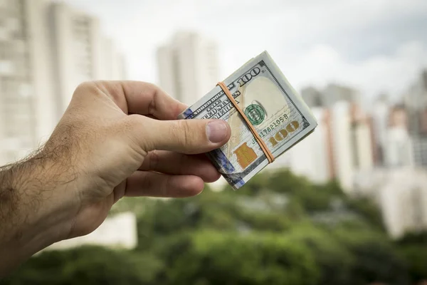 Рука человека с долларовыми купюрами перед городским пейзажем — стоковое фото