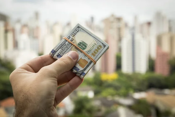 Mano dell'uomo che tiene banconote in dollari davanti a un paesaggio urbano — Foto Stock