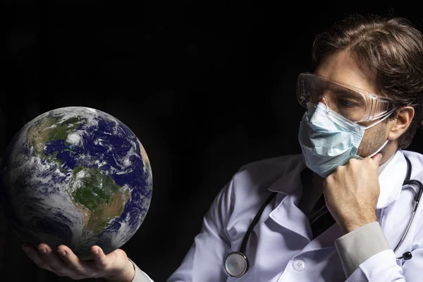 male doctor wearing a mask and goggles with earth in his hands, tired of working with covid-19 on a black background.