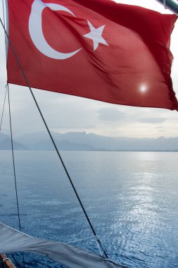 Türk bayrağı suyun üzerindeki rüzgarda dalgalanıyor, Türkiye, hilal ay ve yıldızlı kırmızı bir bayrak, güneş Türk bayrağı boyunca parlıyor