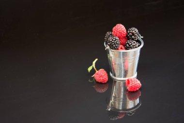 Siyah zemin üzerinde ahududu ve böğürtlen bulunan küçük kova, genel plan