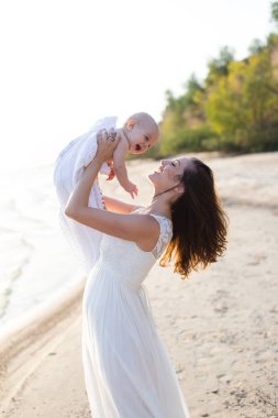 Sahilde denizin kucağında bir bebek tutan genç bir anne