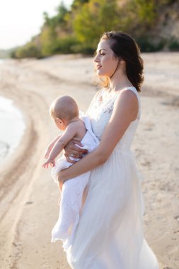 Sahilde denizin kucağında bir bebek tutan genç bir anne