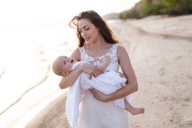 Sahilde denizin kucağında bir bebek tutan genç bir anne