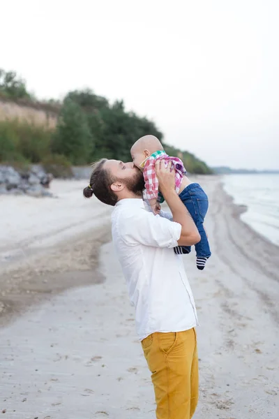 Happy father holding baby in her arms on the beach by the sea — Stock Photo, Image