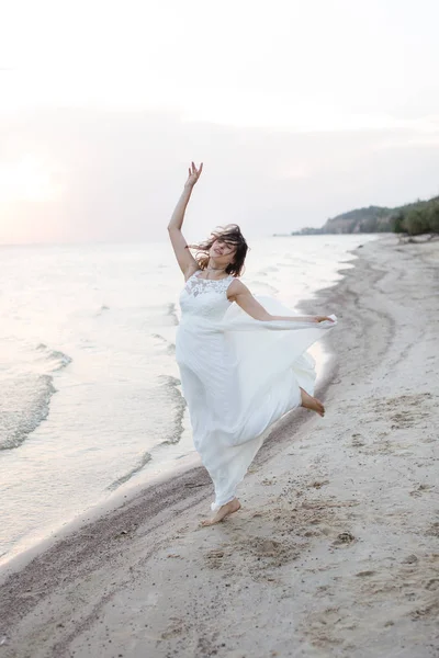 Vacker ung brunett kvinna i vit lång klänning vid havet — Stockfoto