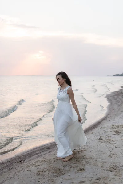 Mulher morena jovem bonita em vestido longo branco na costa do mar — Fotografia de Stock