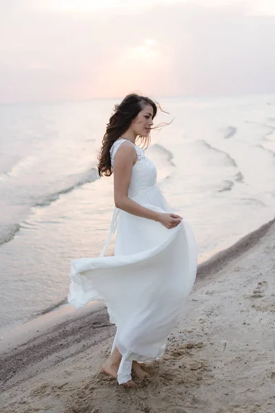 Mulher morena jovem bonita em vestido longo branco na costa do mar — Fotografia de Stock