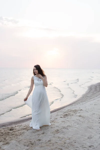 Mulher morena jovem bonita em vestido longo branco na costa do mar — Fotografia de Stock