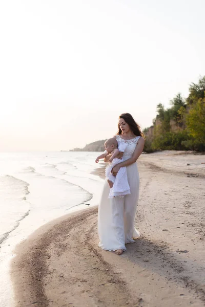 Una giovane madre che tiene un bambino tra le braccia sulla spiaggia in riva al mare — Foto Stock