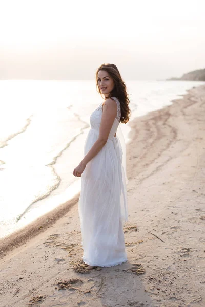 Mulher morena jovem bonita em vestido longo branco na costa do mar — Fotografia de Stock